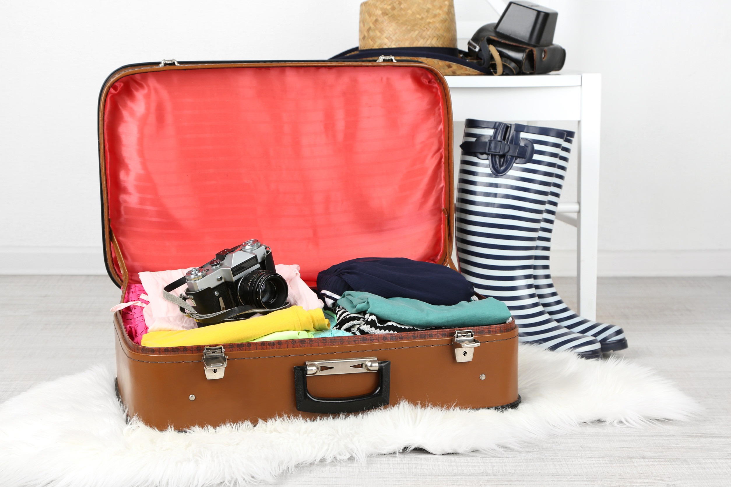 Female clothes and photo camera in old suitcase on light background